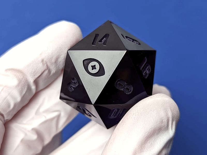 A gloved hand holding a polished black D20