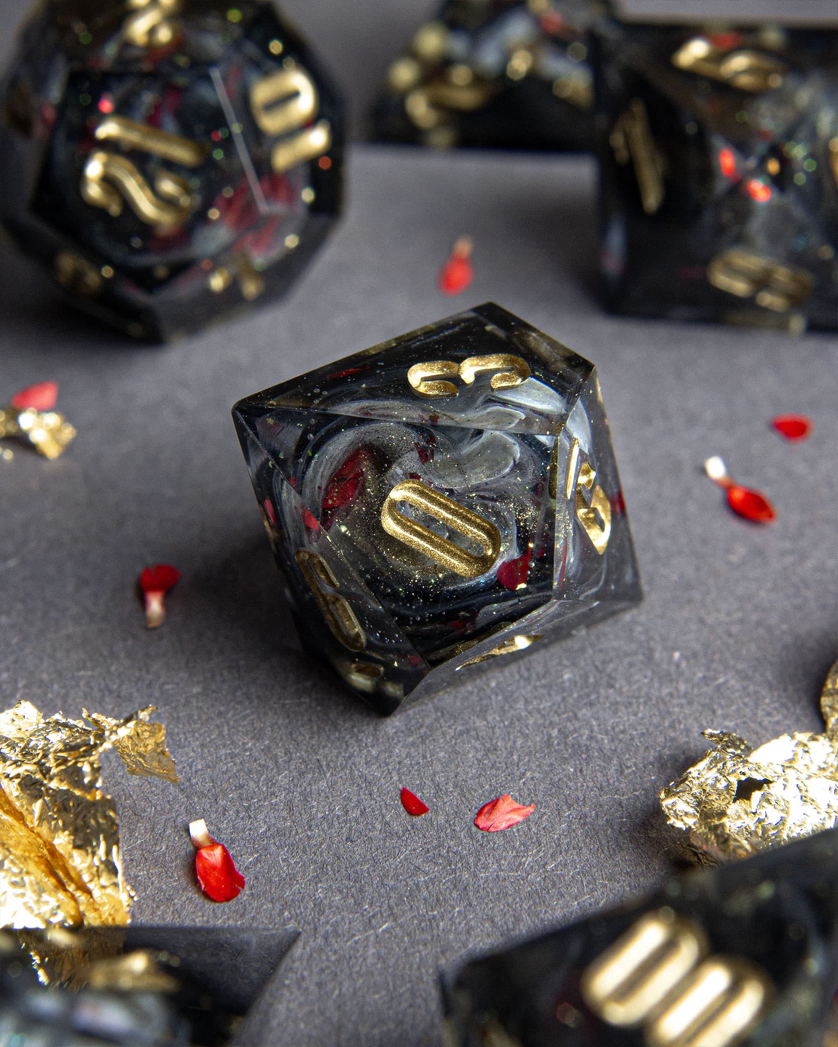 The Last Gommage D10, black resin with gray swirls, red flower petals, metallic foil, and golden numbers