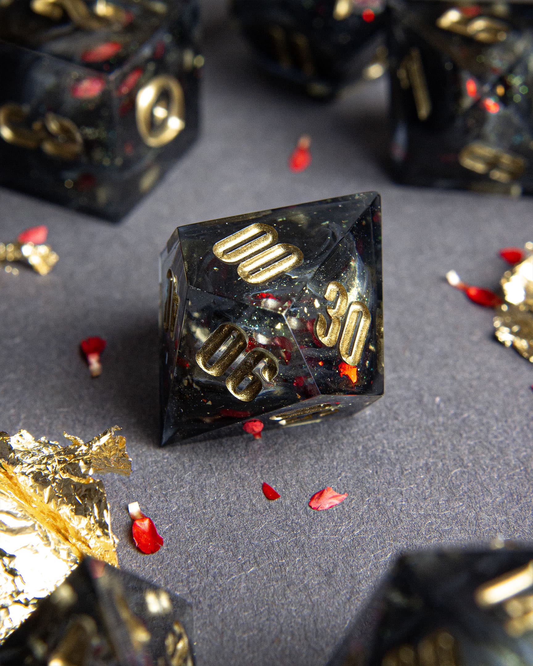 The Last Gommage D100, black resin with gray swirls, red flower petals, metallic foil, and golden numbers