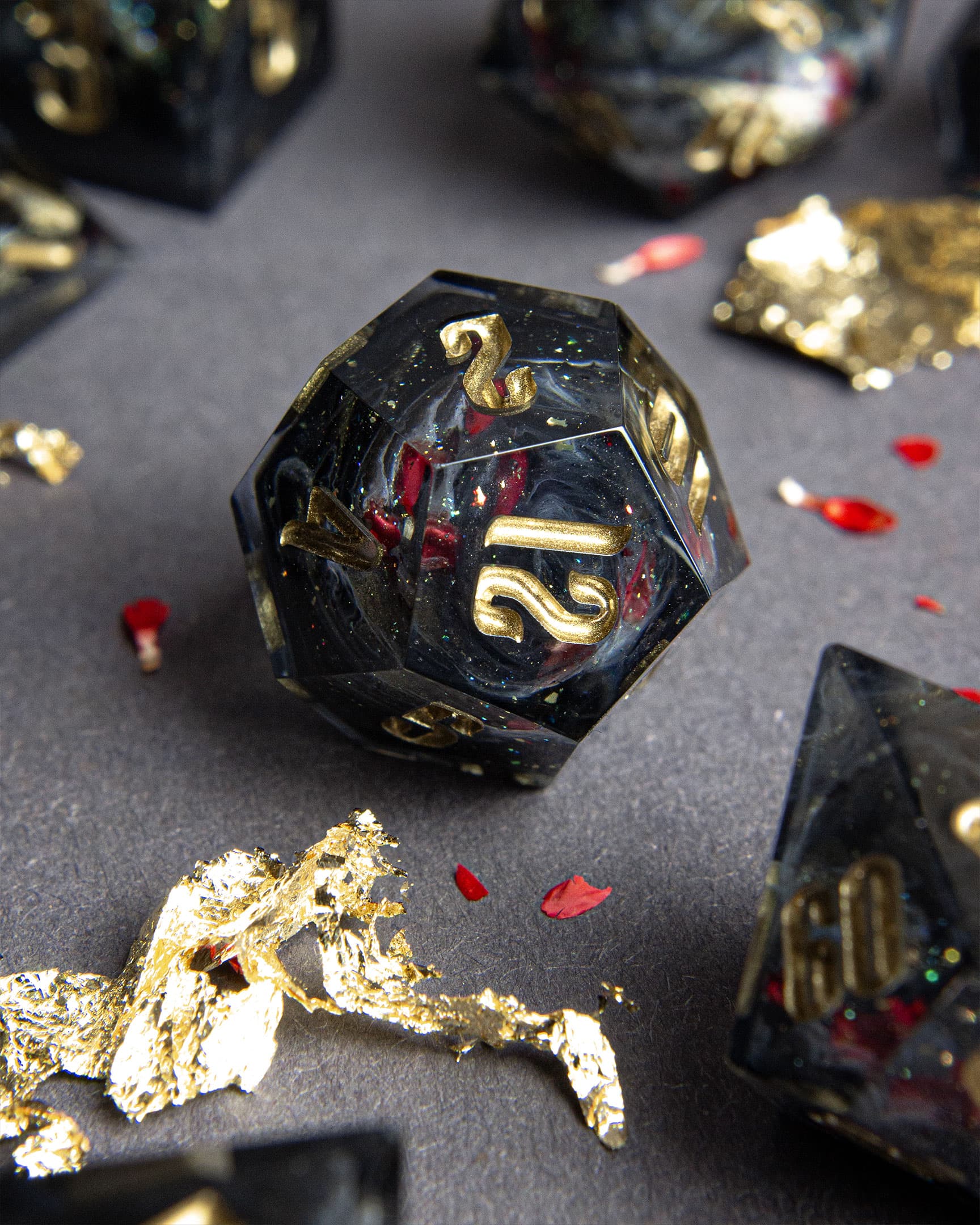The Last Gommage D12, black resin with gray swirls, red flower petals, metallic foil, and golden numbers