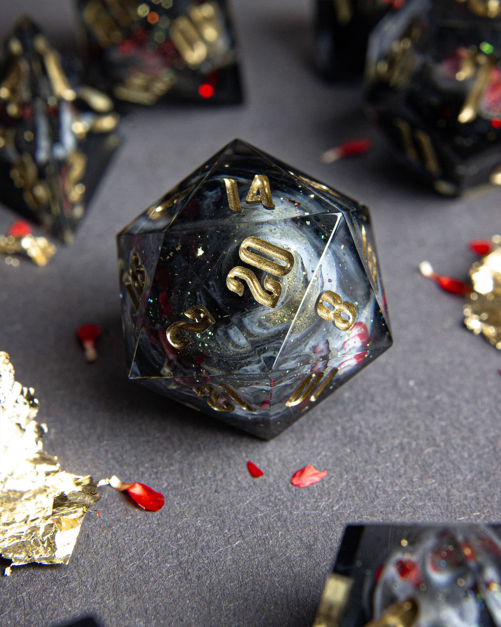 The Last Gommage D20, black resin with gray swirls, red flower petals, metallic foil, and golden numbers