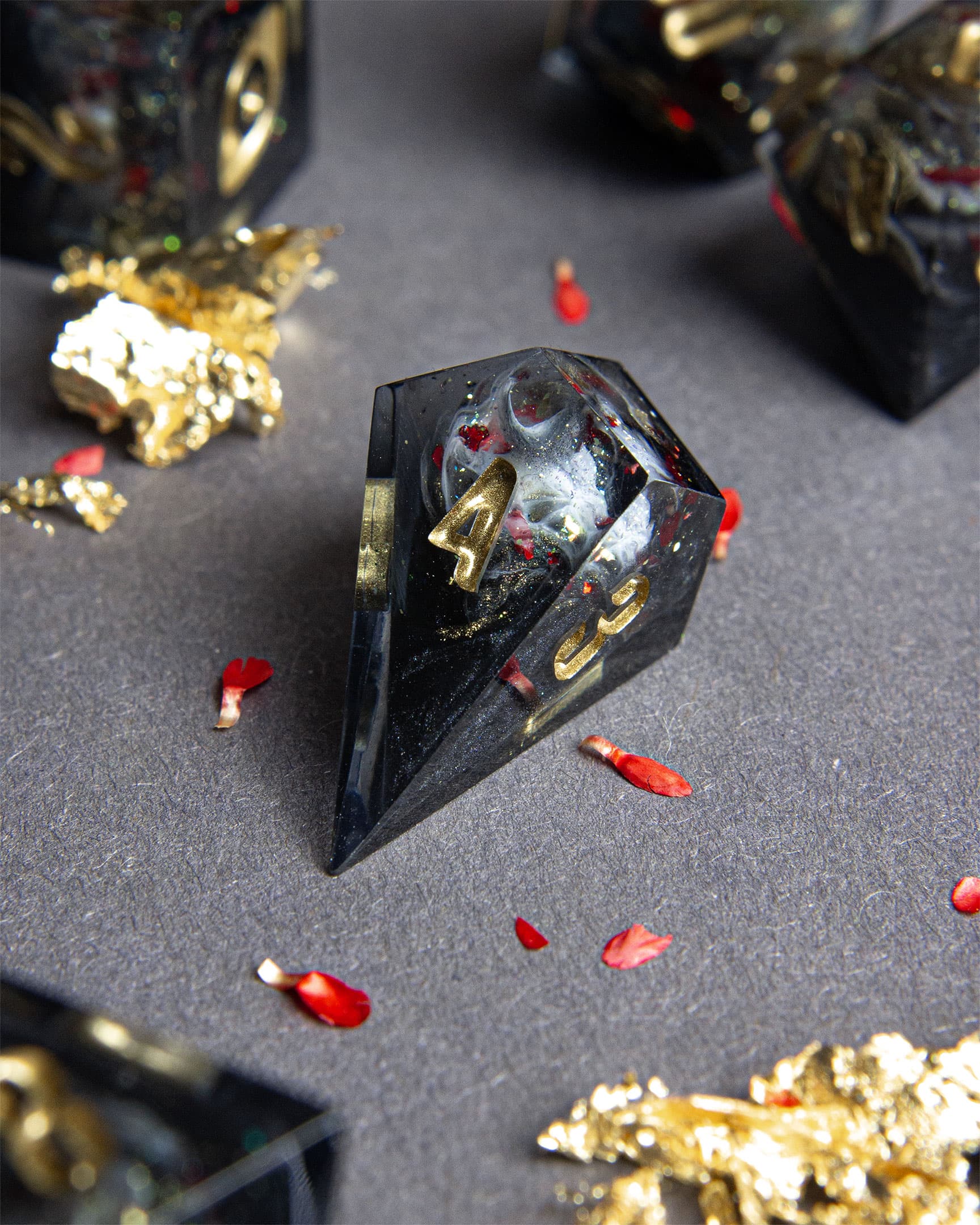 The Last Gommage D4 Shard, black resin with gray swirls, red flower petals, metallic foil, and golden numbers
