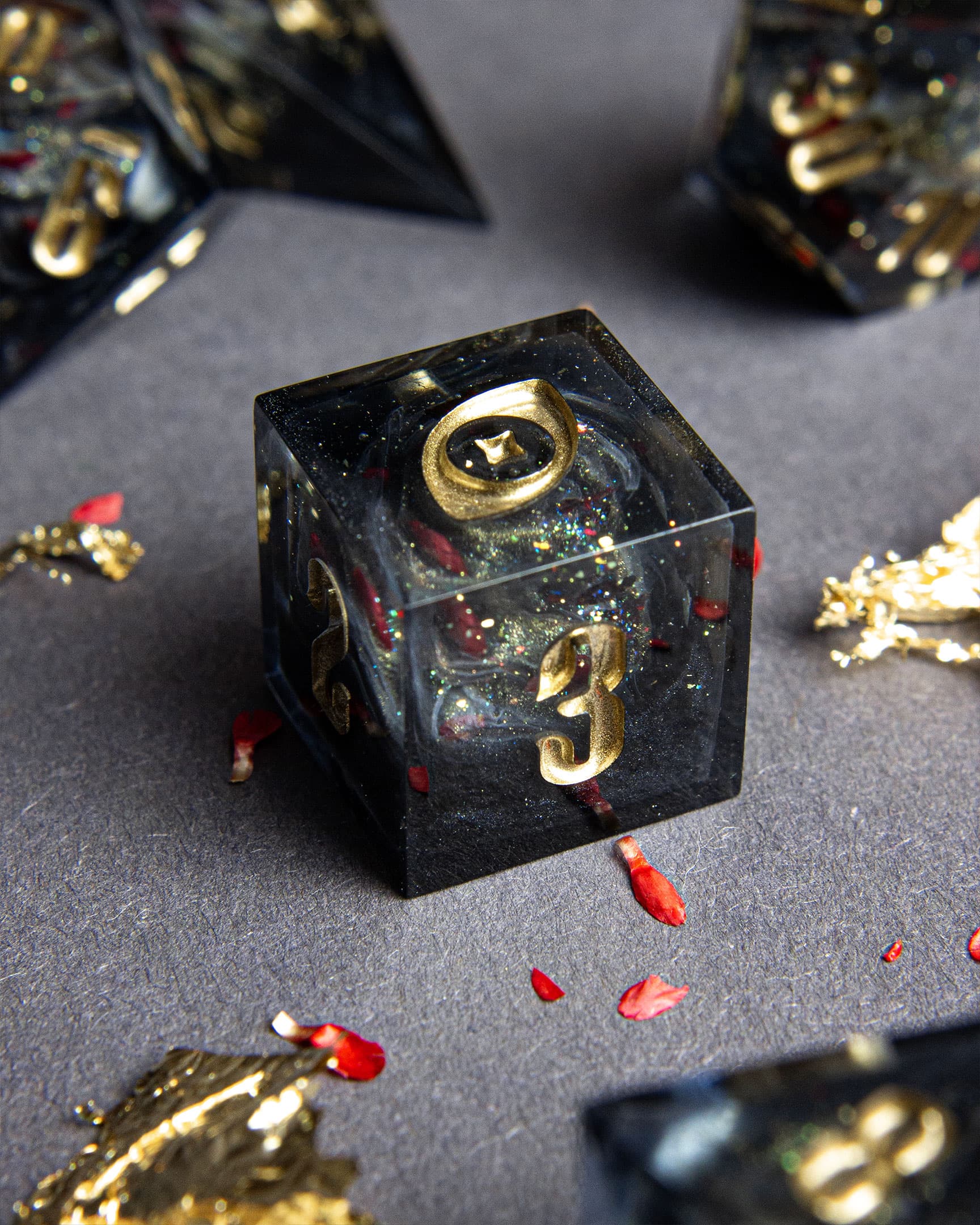 The Last Gommage D6, black resin with gray swirls, red flower petals, metallic foil, and golden numbers