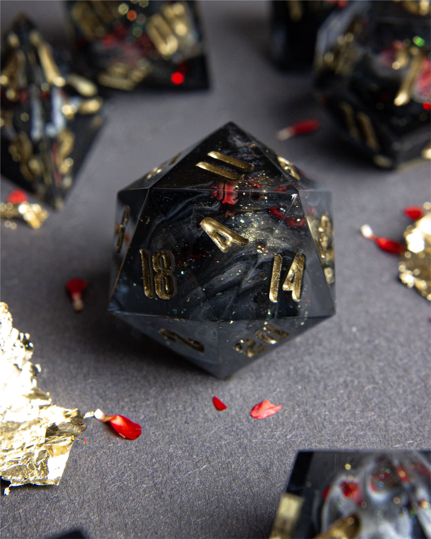 The Last Gommage D20, black resin with gray swirls, red flower petals, metallic foil, and golden numbers